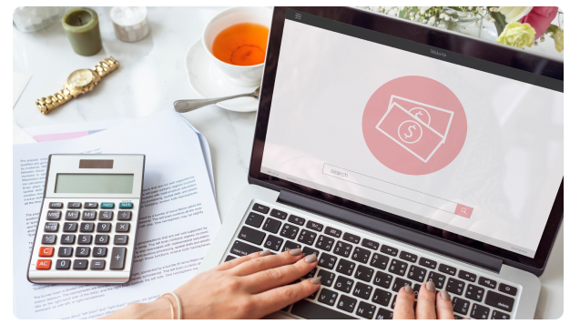 Laptop displaying a money icon beside a calculator and a cup of tea
